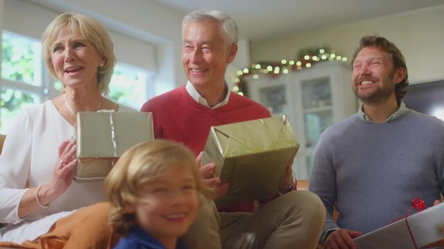 Girl unwrapping present of soft toy dog as multi-generation family exchange gifts around christmas tree at home - shot in slow motion