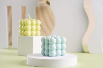 One blue square bubble candle on a white oval and an off-white candle on a cube in the back