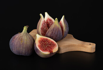 Fresh delicious young whole figs, and cut figs on a wooden cutting board on a black background with reflection