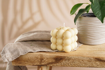 An off-white square bubble candle on a linen cloth on a rustic wooden table with plants at a...