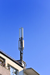 Mobilfunkantenne auf Hausdach vor blauem Himmel 