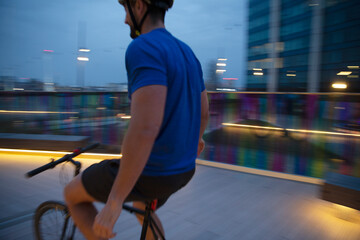 Man riding bicycle on illuminated urban footbridge