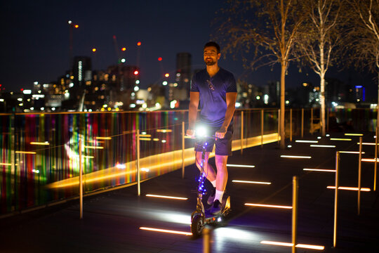 Man riding illuminated scooter in city at night, London, UK