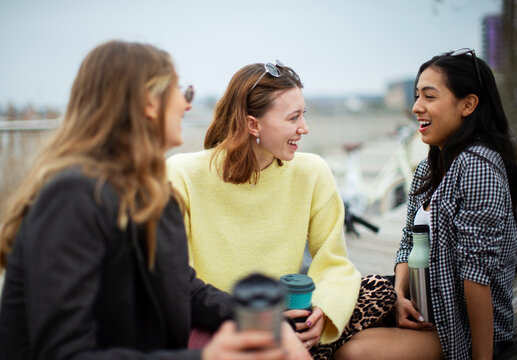 Happy young women friends talking and drinking coffee