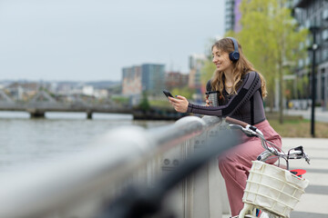 Young woman with headphones using smart phone at urban waterfront