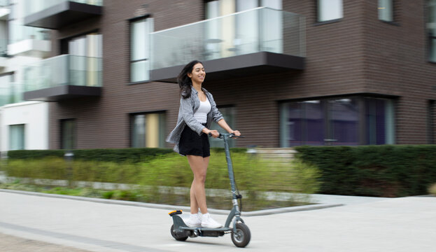 Happy young woman riding electric scooter on urban sidewalk