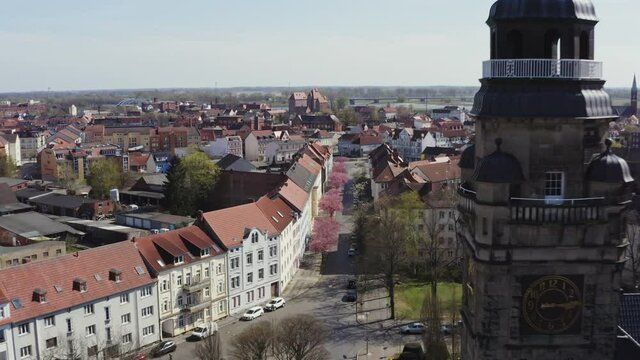The drone flies downwards very close to the tower of the town hall over the roofs of the town of Wittenberge in Brandenburg Germany. The sun is shining and the sky is blue.