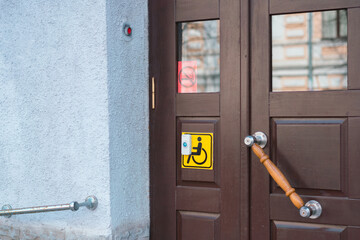 The yellow symbol of wheelchair and door bell near stairs in the house. Disability. Wooden door. Entrance. Entry