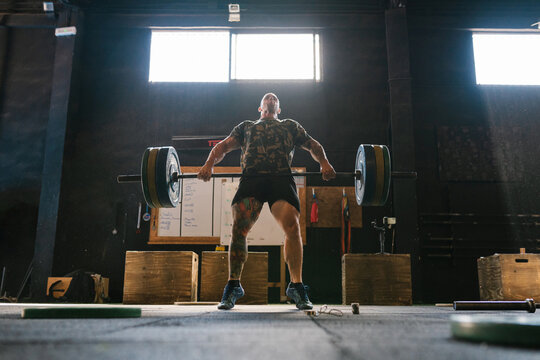 Muscular man lifting barbell in light gym