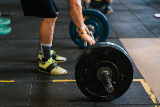 Crop male athlete touching barbell on floor