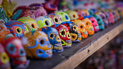 Row of miniature hand painted dia de muertos sugar skulls festival art on wood shelf at local open market in California