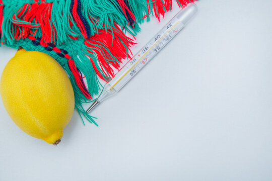 A warm winter scarf, thermometer, lemon lie on the side on a white background with a place for text. High quality photo