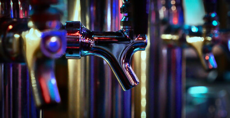 Row of silver metal beer tap faucets in local night club dive bar