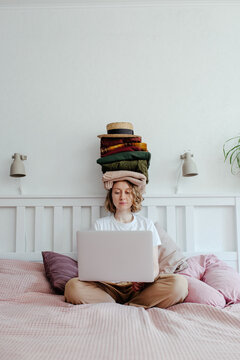 Woman with stack of clothes using laptop