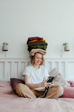 Woman with stack of clothes using smartphone