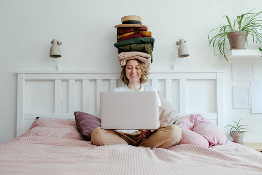 Woman with stack of clothes using laptop