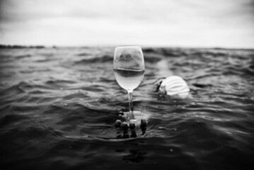 Surreal concept photography. Swimmer holding a glass of wine in the sea