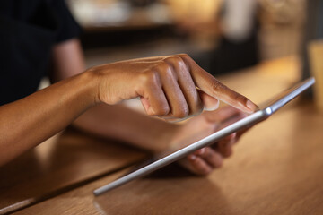 Crop black woman browsing tablet at table in cafe