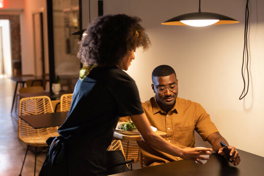 Black waitress serving food for client in restaurant