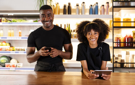 Cheerful black waiter and waitress using gadgets in cafe