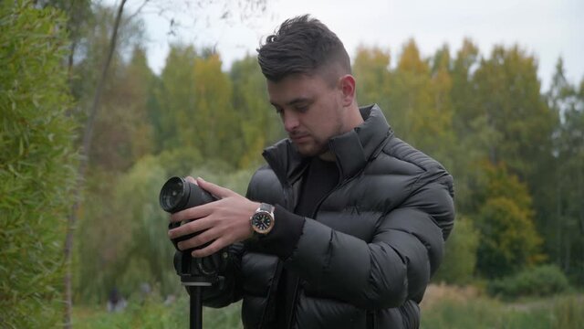 Close up shot of an  attractive caucasian photographer in black outfit taking pictures with the green park background