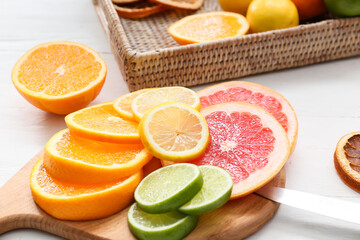 Board with slices of different citrus fruits on light wooden background, closeup