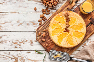 Board with tasty orange pie with almond nuts and glass of juice on light wooden background