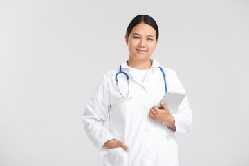 Portrait of female Asian doctor with tablet on light background