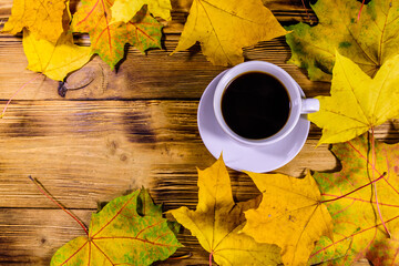 Cup of coffee and heap of yellow maple leaves on a wooden table. Top view