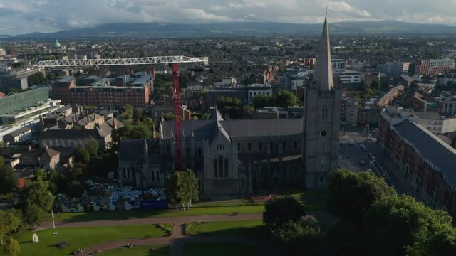 Slide and pan footage of old stone church surrounding park and town in background. Red and white tower crane. Dublin, Ireland