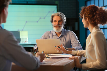 Mature businessman working with team in office at night