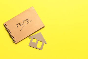 Notebook with word RENT and cardboard house on yellow background