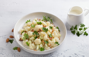 Cauliflower salad with apples, almonds, herbs and yogurt dressing on light gray textured background. Healthy homemade diet food