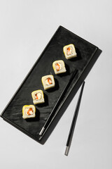 Plate with delicious sushi rolls and chopsticks on light background