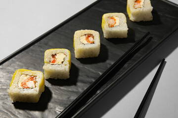 Plate with delicious sushi rolls and chopsticks on light background, closeup