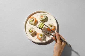 Woman taking delicious sushi roll from plate on light background