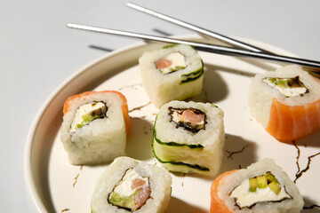 Plate with delicious sushi rolls and chopsticks on light background, closeup