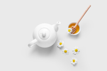 Teapot, honey and chamomile flowers on white background