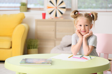 Cute little girl with ponytails sitting at table in living room