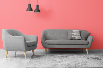 Grey armchair with sofa and black lamps hanging near pink wall