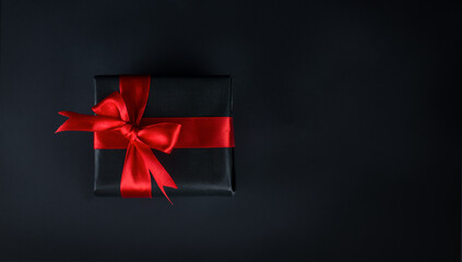 Black gift with red ribbon on black background