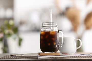 Mason jar of ice coffee and magazine on table in room