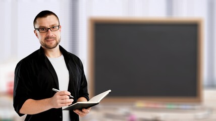 Online schooling. Positive male teacher standing near empty blackboard