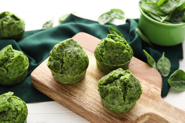 Board with tasty spinach muffins on light wooden background