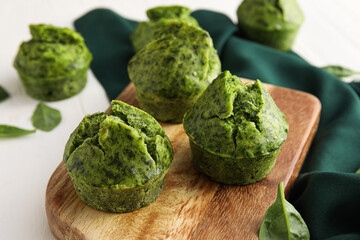 Wooden board with tasty spinach muffins on light background, closeup