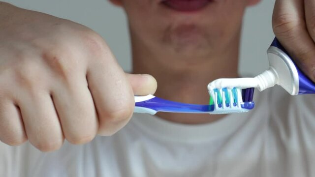A male hands squeeze toothpaste onto a toothbrush close-up.