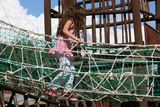 Little girl in playground. Rope and wooden bridge for children. Outdoor park games. Outdoor fun. Games with protective elements for children. Game with security measures. Outdoor. Sunny day. 