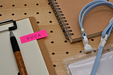 There is a sticky note with the letters VUCA stamped on the edge of a clipboard placed along with a...