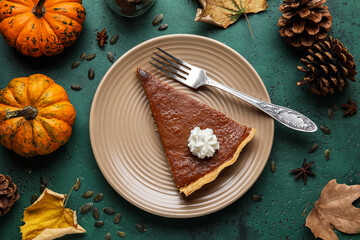 Autumn composition with piece of tasty pumpkin pie on green background