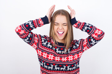 Young caucasian girl wearing christmas sweaters on white background goes crazy as head goes around...